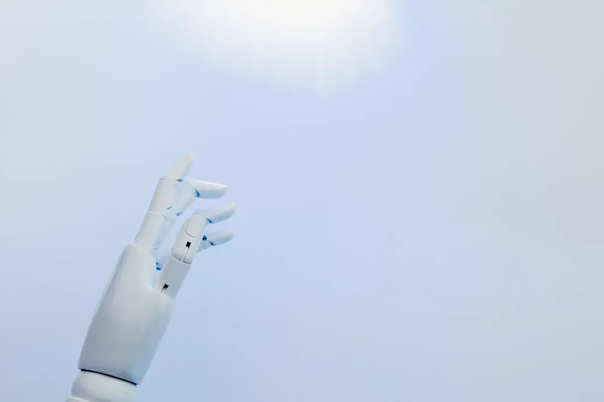 白い背景上に明るい光に向かうロボットの手。これは革新を象徴している。