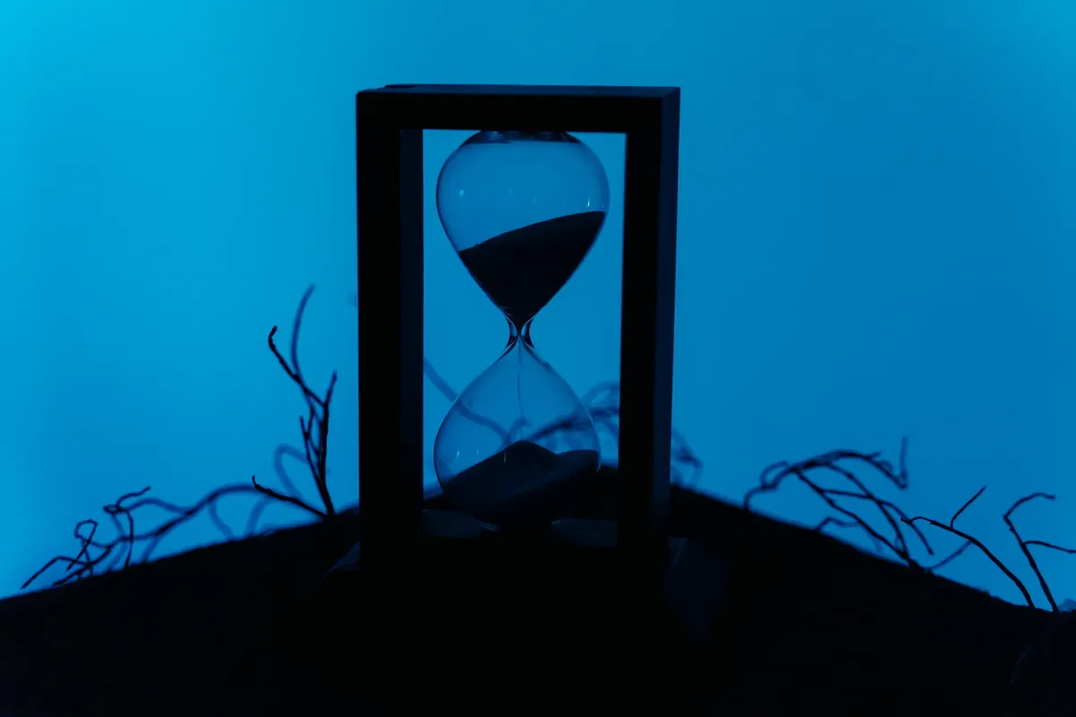 A silhouette of an hourglass set against a vivid blue background, highlighting the passage of time.