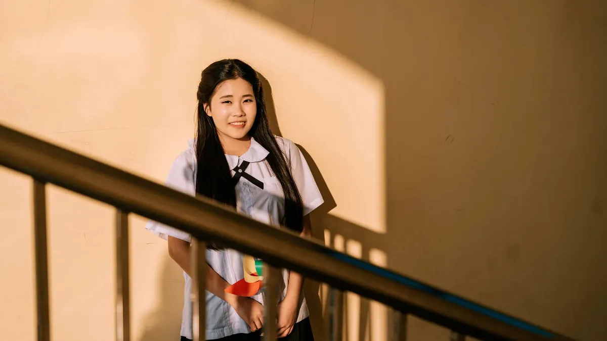 Woman in school uniform standing against a wall in warm sunlight.