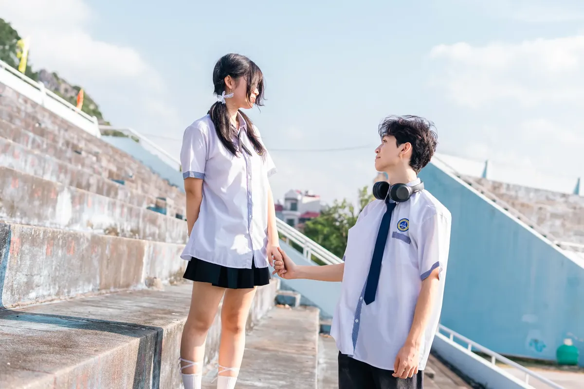 Teenagers in school uniforms hold hands outdoors on sunny day.