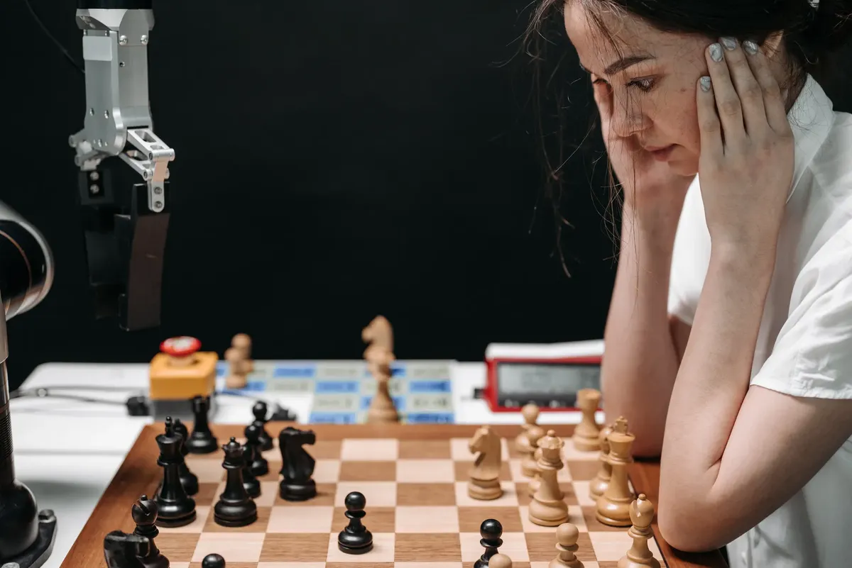 A woman engaged in a thought-provoking chess game with a robotic opponent.