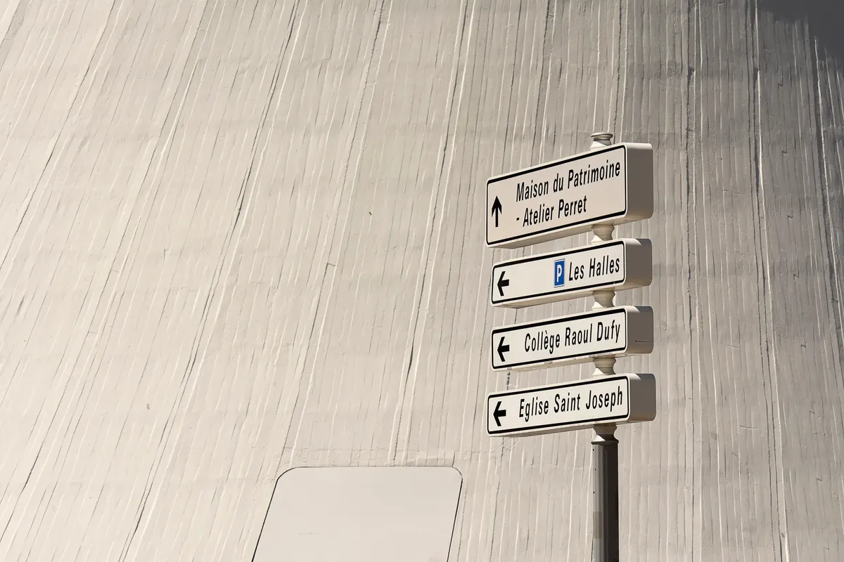 Directional signs in a cityscape setting with modern architectural backdrop.