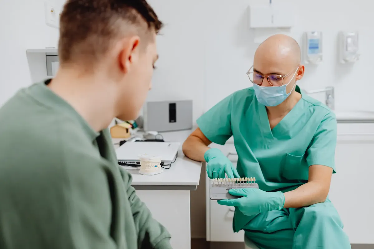 Dentist in scrubs showing a shade guide to patient for dental evaluation.
