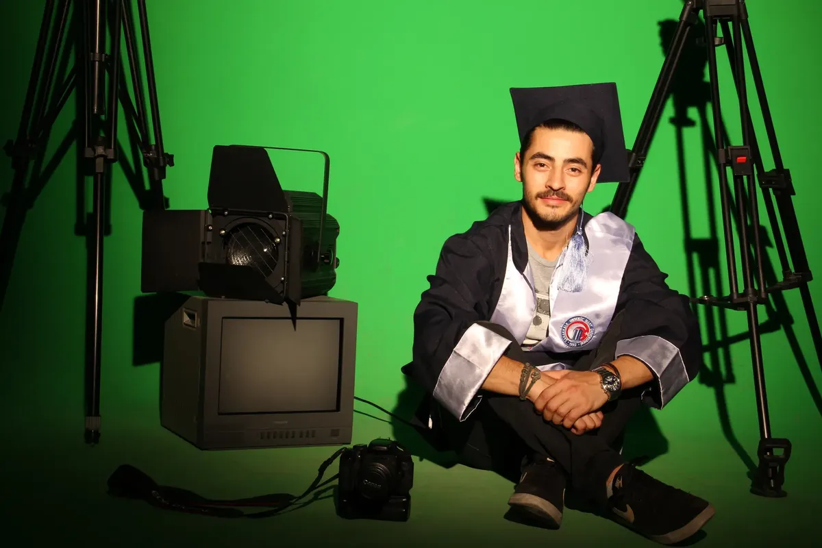 Graduate in studio setting with camera equipment, symbolizing creative future paths.