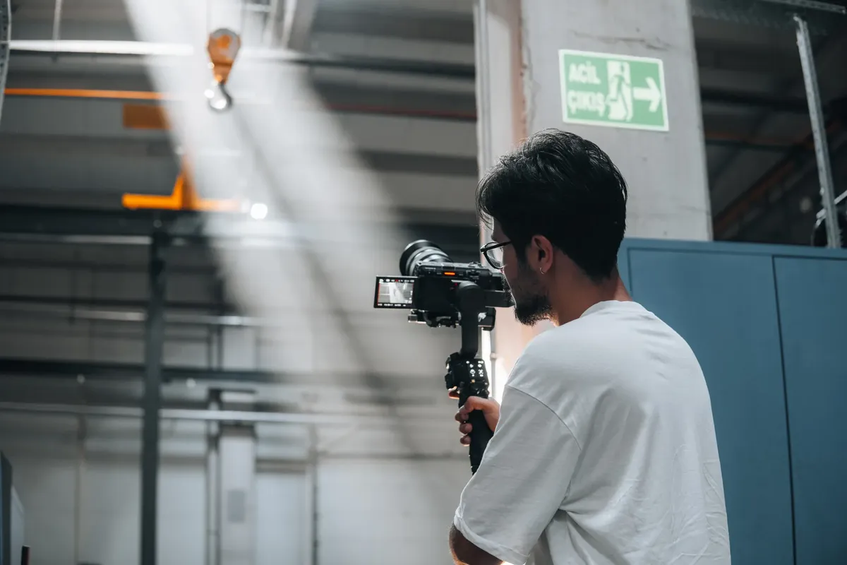 Cameraman using a gimbal to record a scene in an industrial interior space.