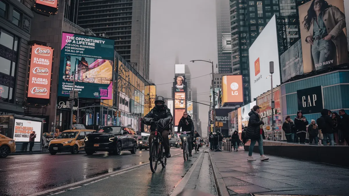 A lively evening scene in Times Square, New York City, with cyclists and vibrant advertisements.