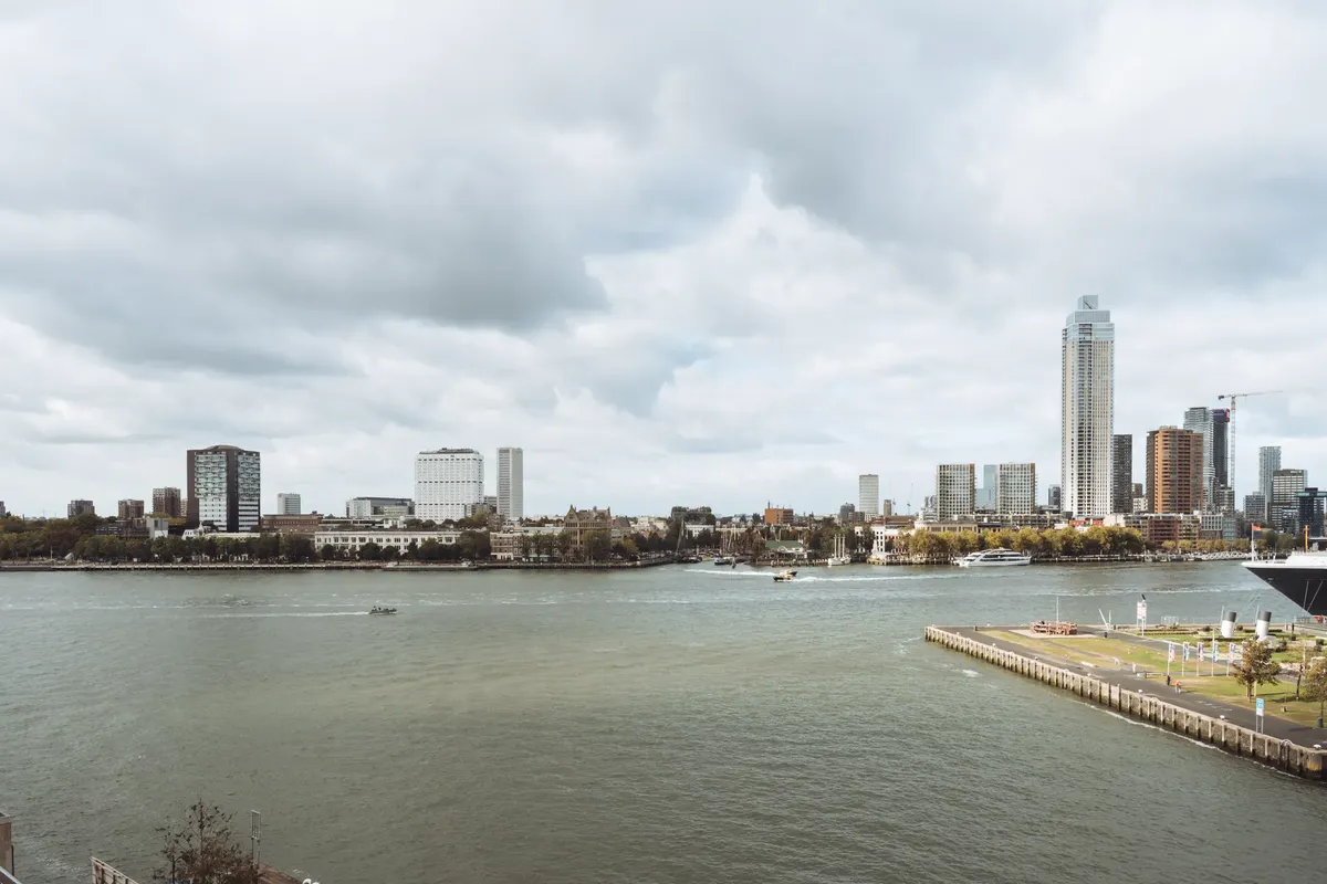 Scenic view of Rotterdam's modern skyline along the river under cloudy skies.
