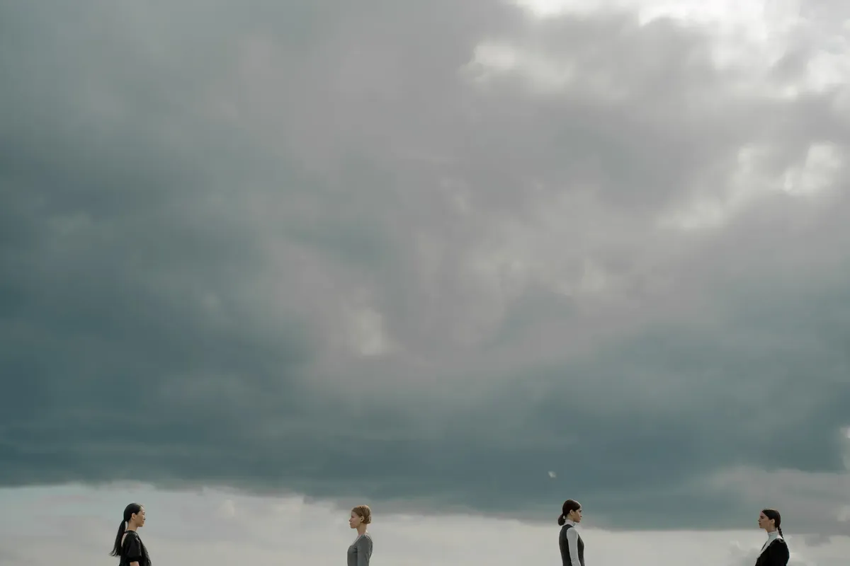 Four people beneath dramatic cloudy skies, evoking modern social themes.