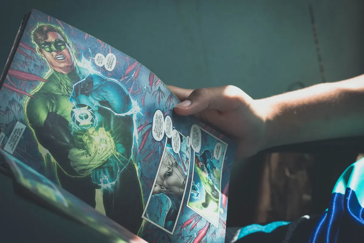 From above of crop anonymous person reading interesting comic book while sitting on chair at home