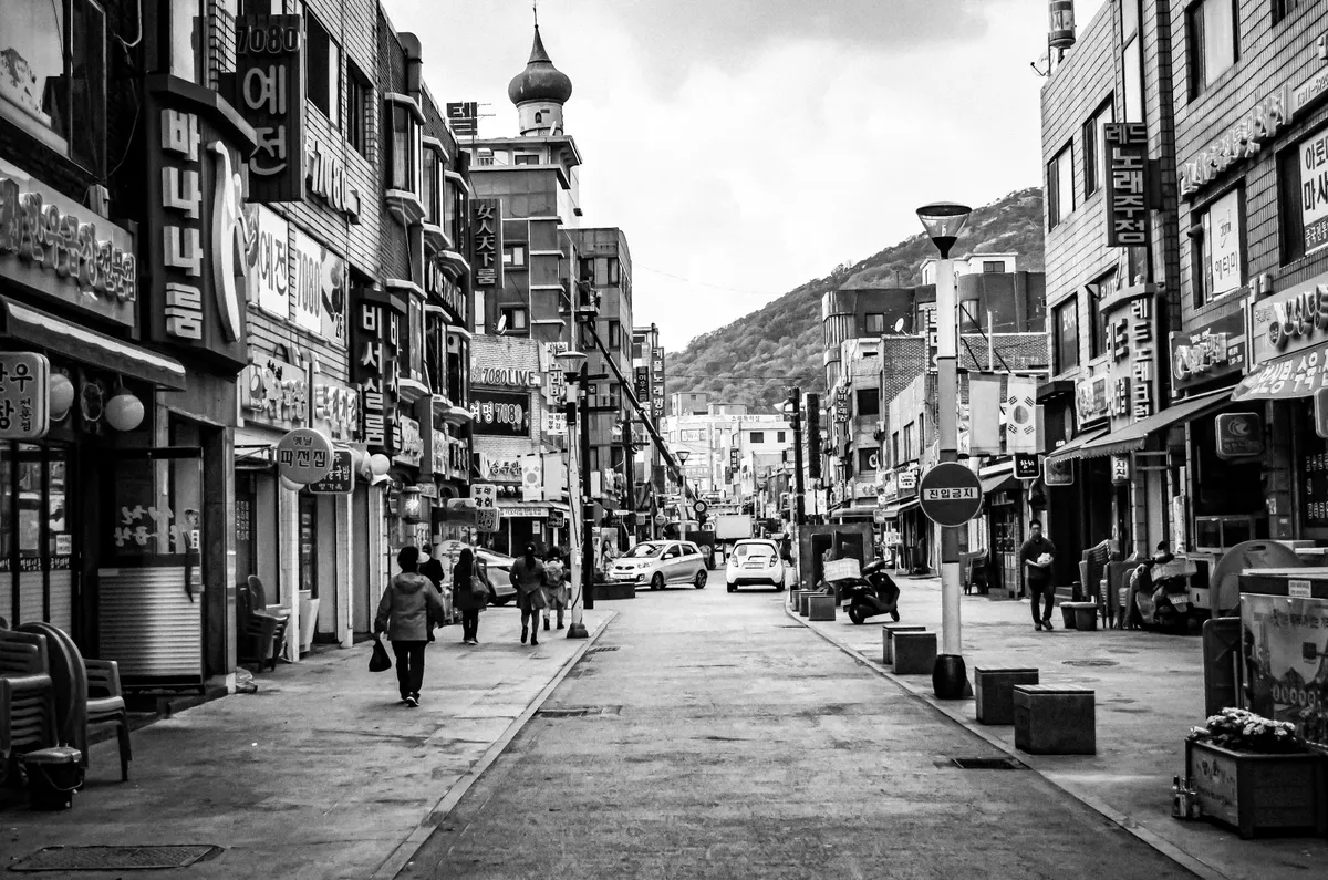 A bustling street in Korea featuring shops and pedestrians in a black and white composition.