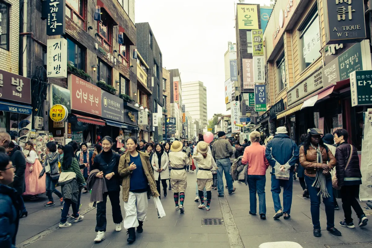 Vibrant city street in Korea with diverse people and shops. Captures urban life.