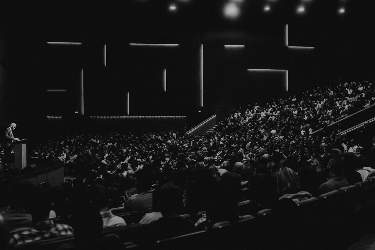 Black and white photo of a large audience in an auditorium with a speaker at the lectern in Oradea.