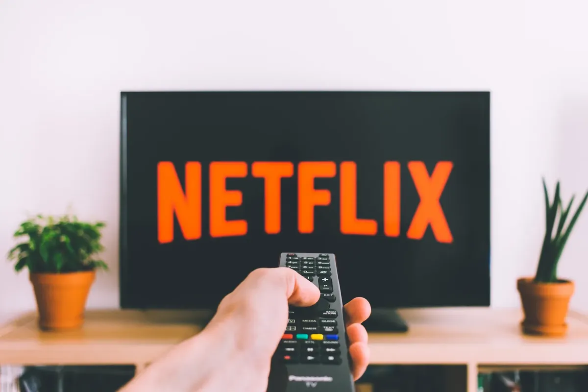 手拿電視遙控器，面對螢幕上的Netflix。適合流媒體與電影之夜主題。