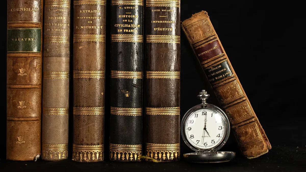 A collection of antique books with a vintage pocket watch on a black background.