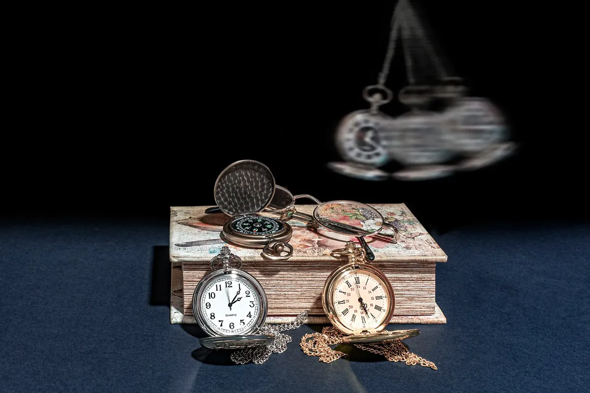 A collection of vintage pocket watches and a compass on a decorative book, evoking a retro feel.